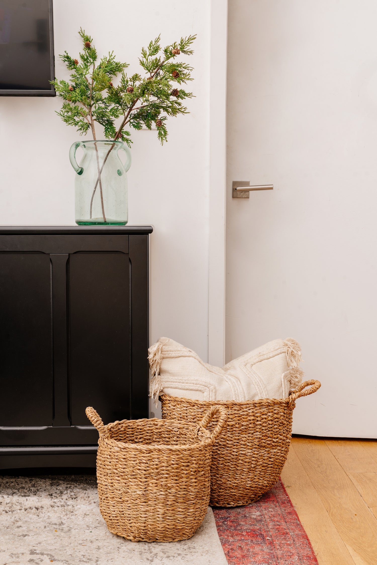 Set of two brown woven baskets on rug, next to black cabinet.