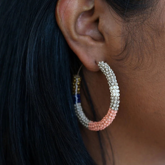 Gold hoop beaded earrings wrapped with glass beads in dusty pink, navy blue, cool taupe and gold colors shown on woman's ear.