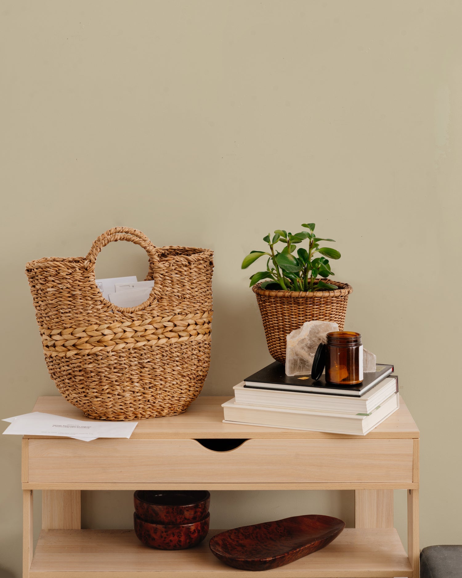 Brown woven basket with round handles on brown table with books and plant.