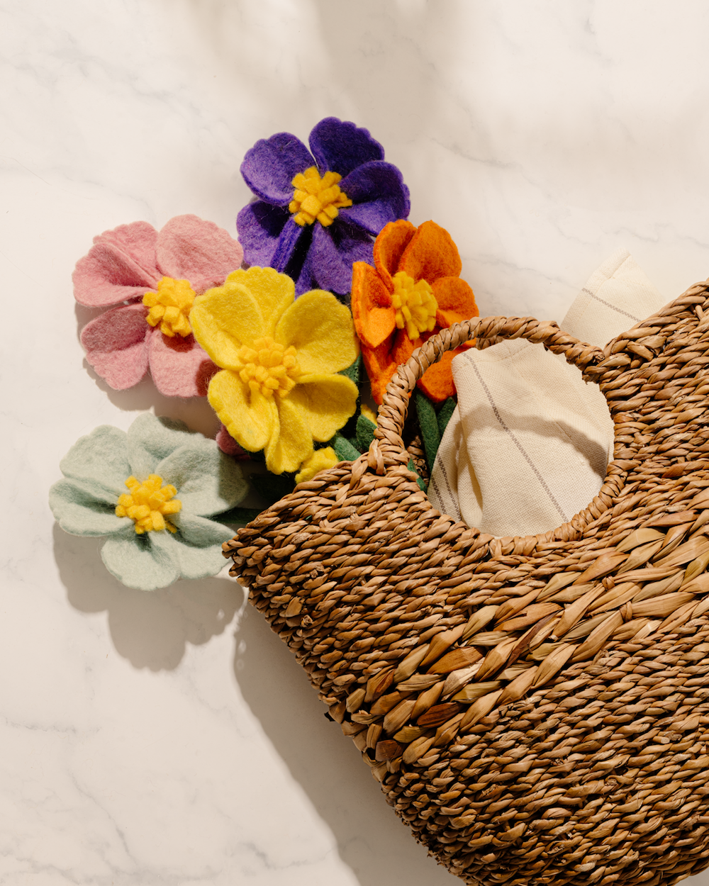 Closeup of brown woven basket with round handles and felt flowers.