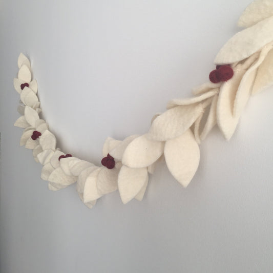 Felt garland with white leaves with red berries hanging on wall.