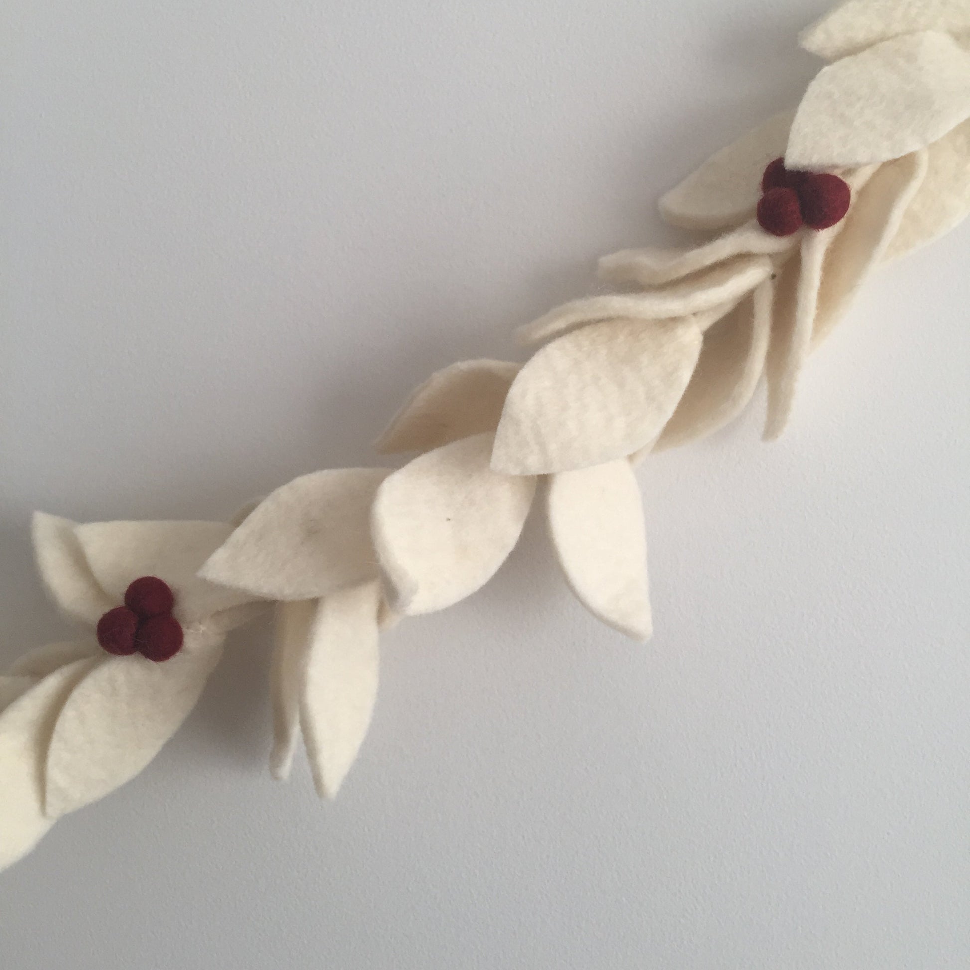 Felt garland with white leaves with red berries hanging on wall.