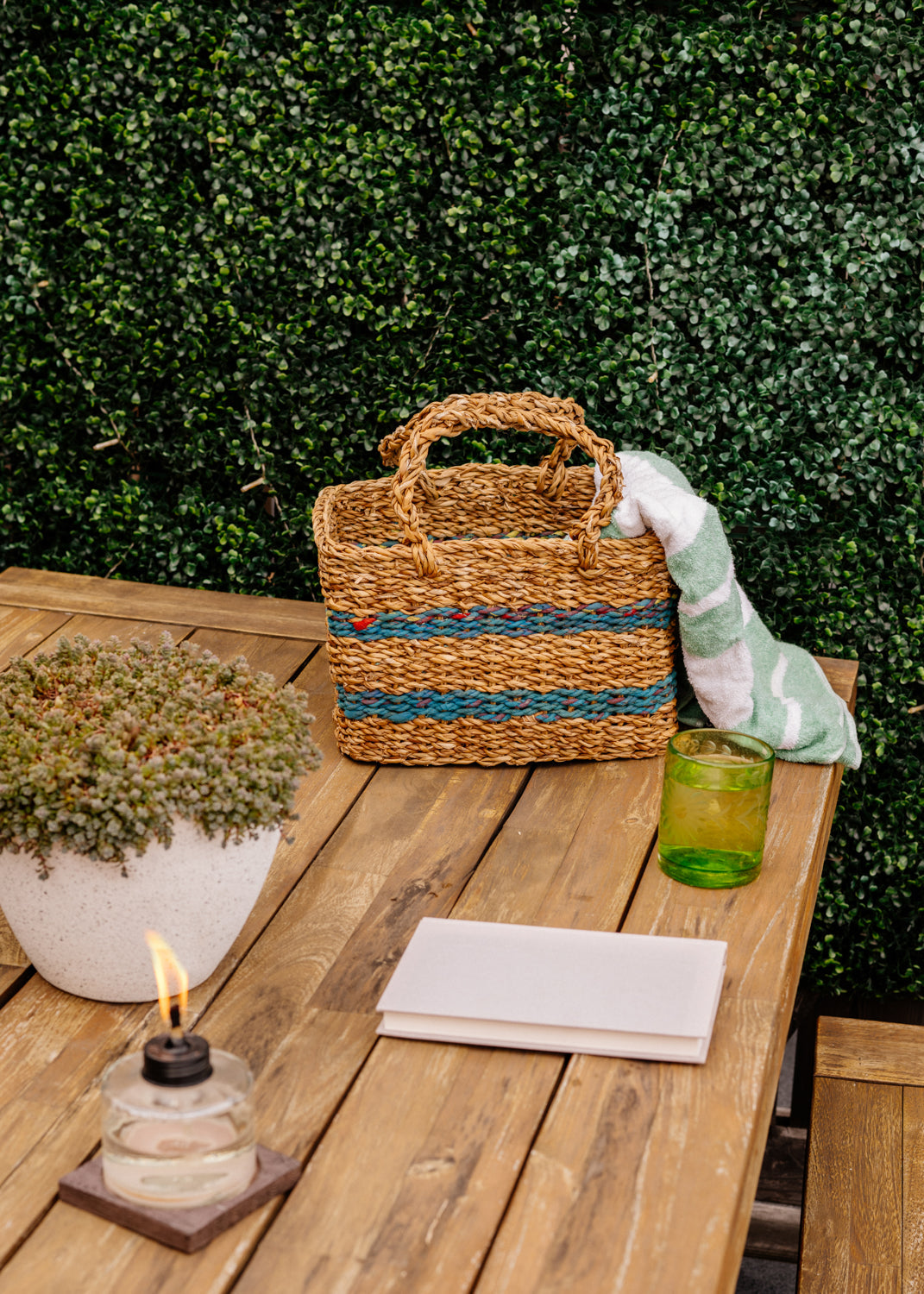 Woven brown basket with green stripes, standing on brown picnic table.