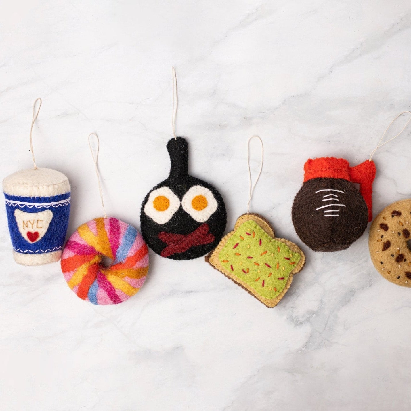 Felt ornament of a coffee cup with a blue sleeve that has NYC and a red heart on it scattered with other various food ornaments.