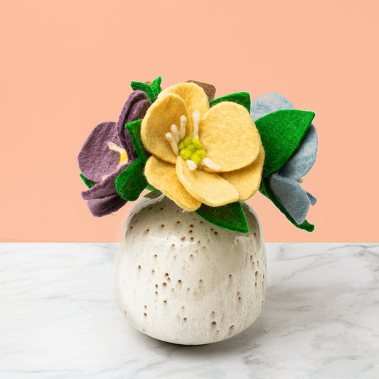 Purple, yellow, and blue felt Hepatica flowers in a tan round vase.