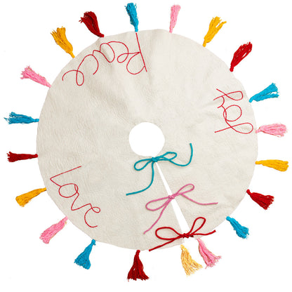 Top view of white felt Christmas tree skirt with multicolored tassels around the edges and the words "peace" "love" and 'joy' embroidered.