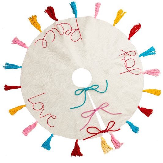 Top view of white felt Christmas tree skirt with multicolored tassels around the edges and the words "peace" "love" and 'joy' embroidered.