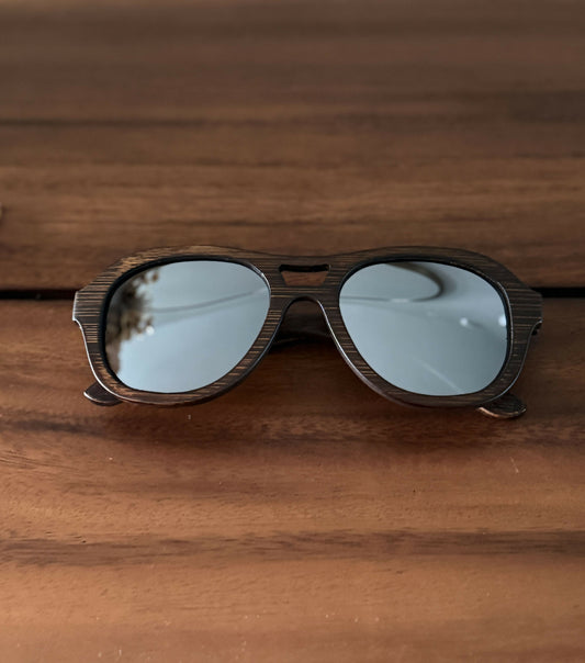 Avion style dark brown bamboo sunglasses with mirrored lenses sitting on dark wood.