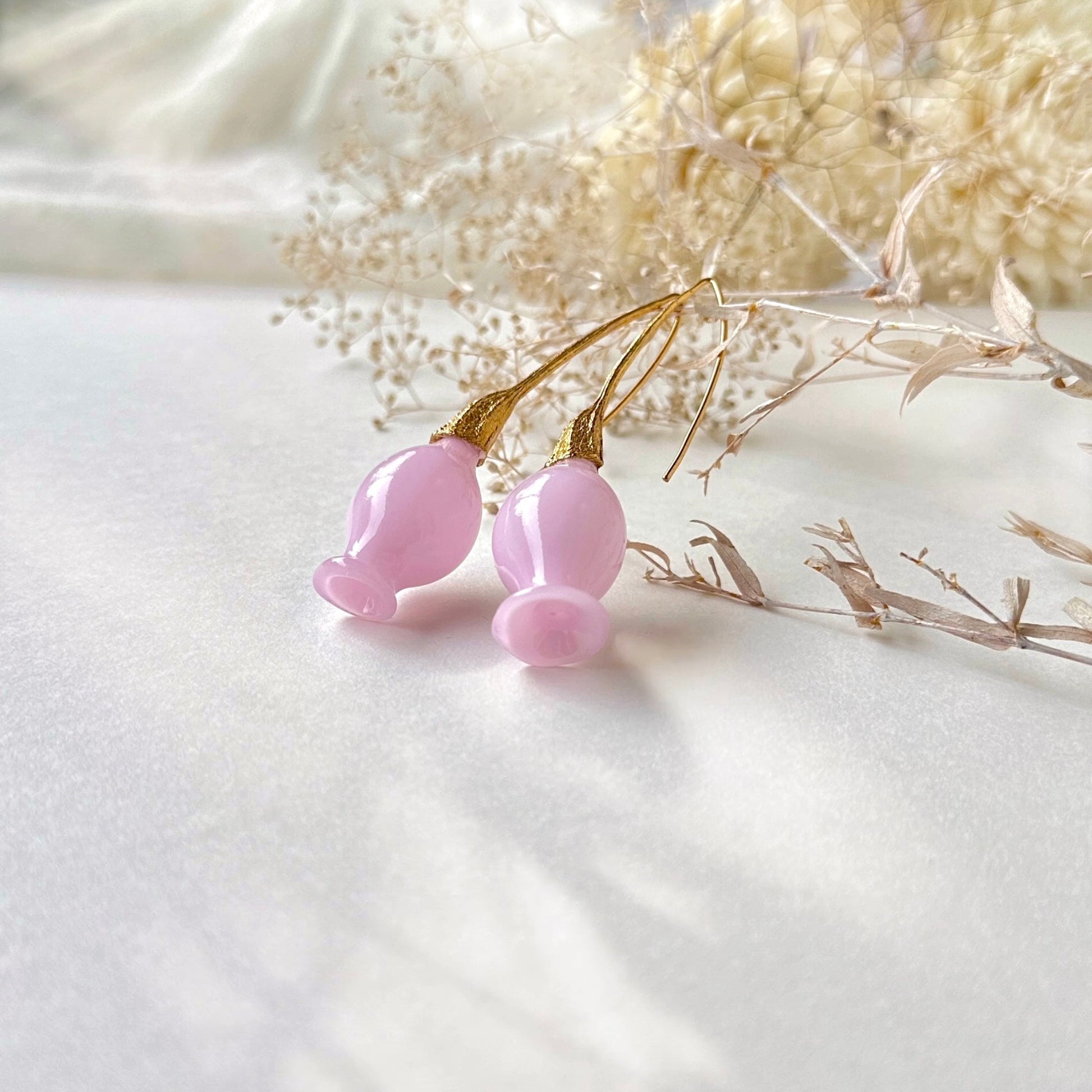 Pair of pink glass earrings with gold plated findings. Dried flowers in upper area of image.