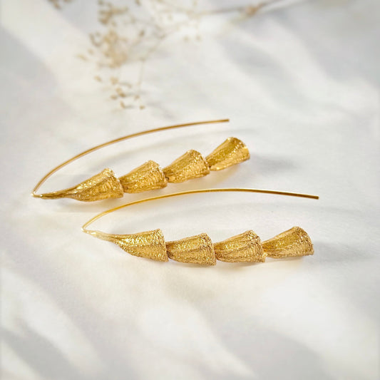Pair of gold plated dangle earrings laying on side.