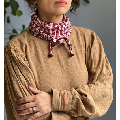 Partial view of woman wearing brown woven long sleeve shirt with red and white bandana, arms crossed in front.