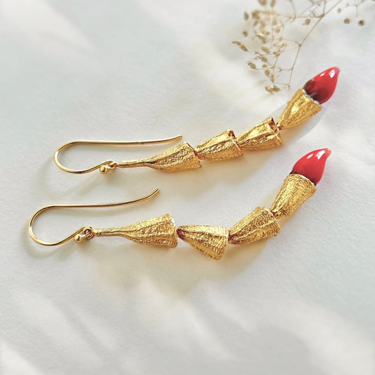 Pair of red and gold chili pod earrings with gold plated findings, laying on side.