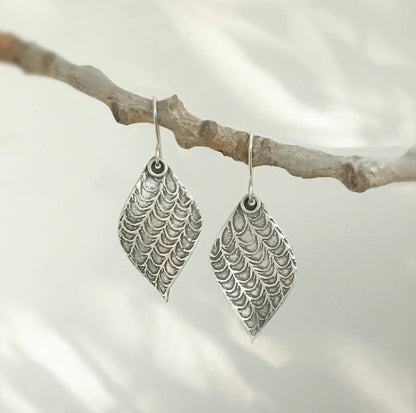 Pair of silver leaf earrings hanging from branch.