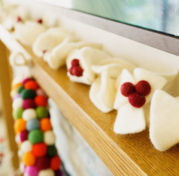 Felt garland with white leaves with red berries close up on wood mantel.