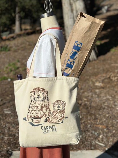 Canvas tote bag with picture of a momma otter and pup, and carmel-by-the-sea written below on the shoulder of a manikin.