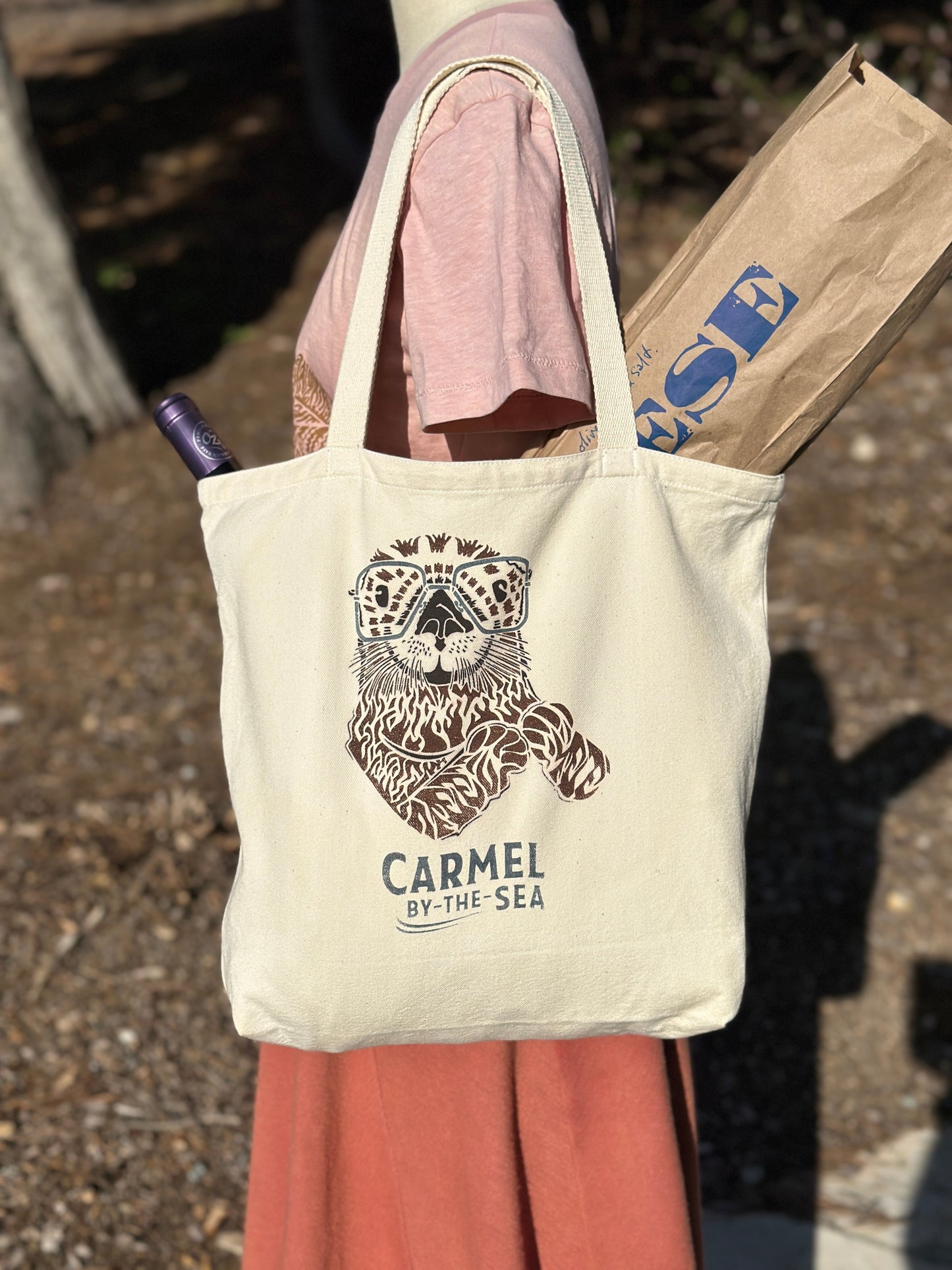 Canvas tote bag with picture of an otter and carmel-by-the-sea written below, on the shoulder of a manikin.