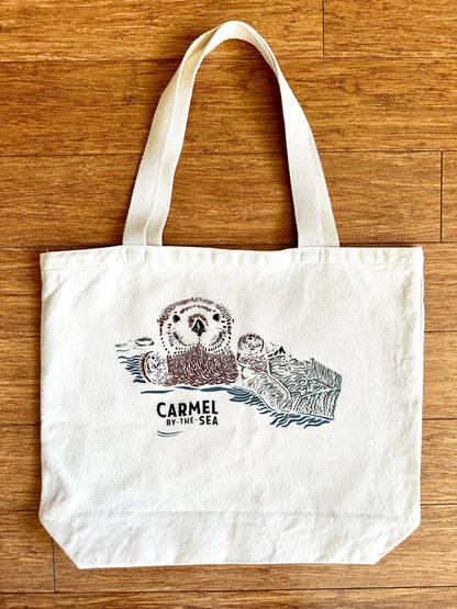 Canvas tote bag with picture of otter pup wrapped in seaweed, and carmel-by-the-sea written below.