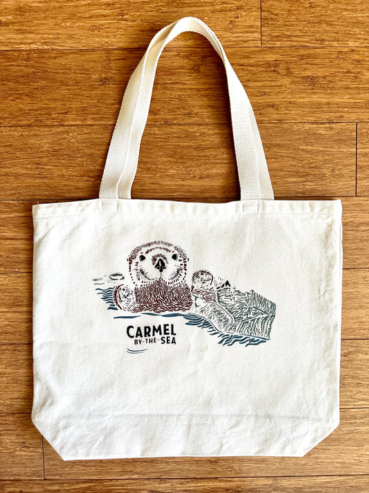 Canvas tote bag with picture of otter pup wrapped in seaweed, and carmel-by-the-sea written below.