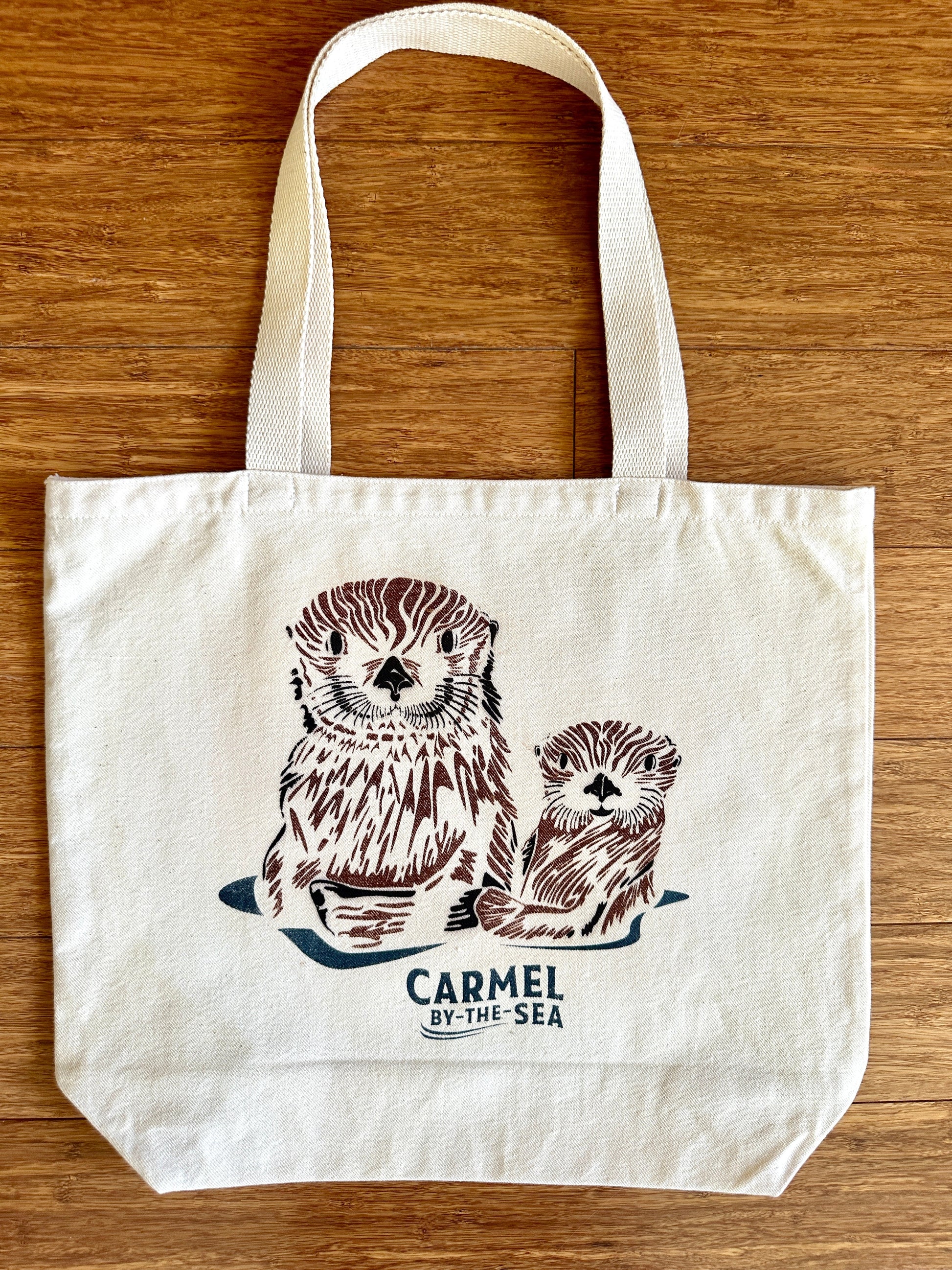Canvas tote bag with picture of a momma otter and pup, and carmel-by-the-sea written below.