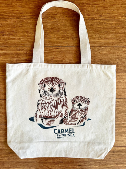 Canvas tote bag with picture of a momma otter and pup, and carmel-by-the-sea written below.