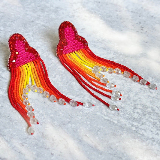 Pair of red, orange, yellow tassel earrings on grey background.