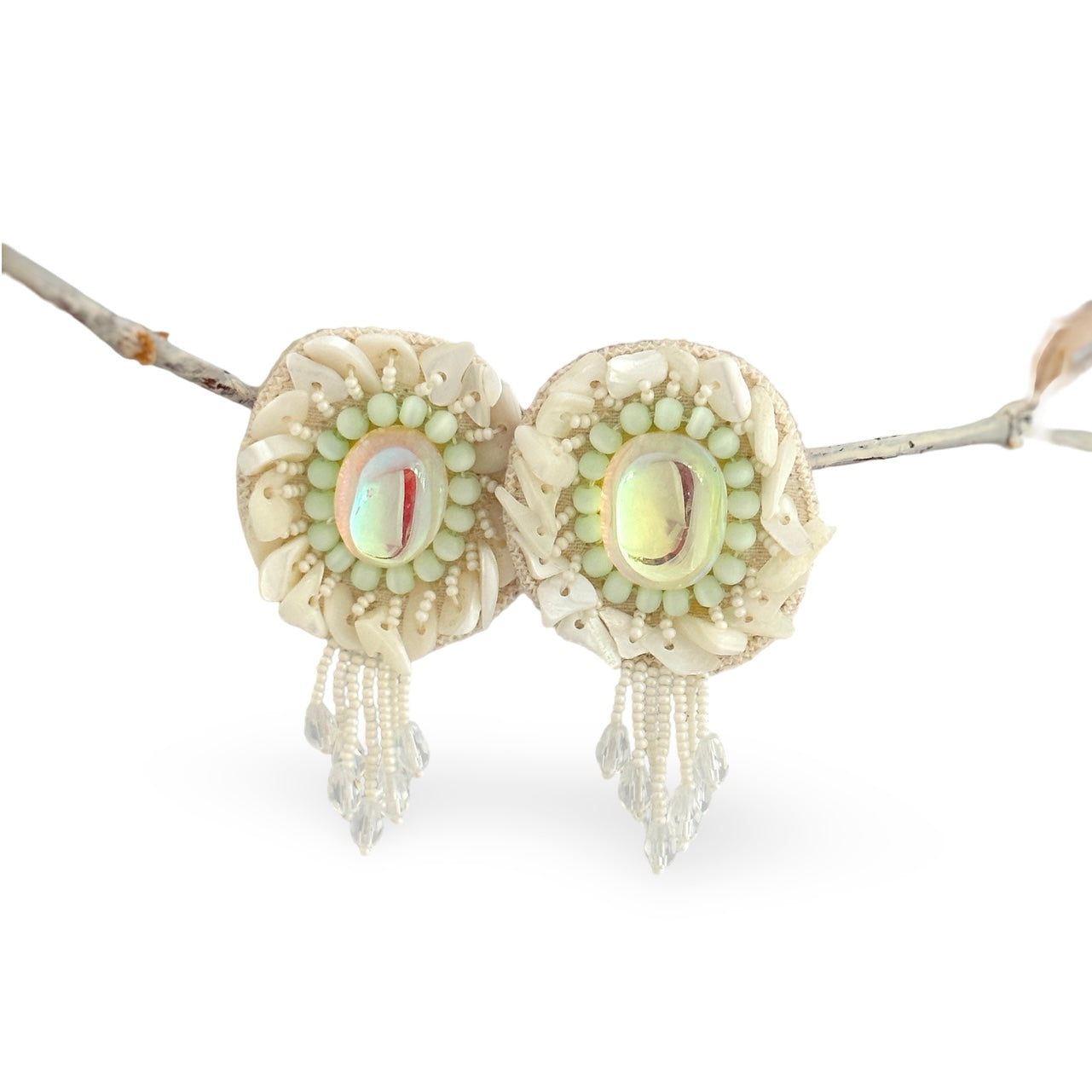Pair of iridescent white earrings with pink and blue accents hanging from rope.