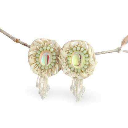 Pair of iridescent white earrings with pink and blue accents hanging from rope.