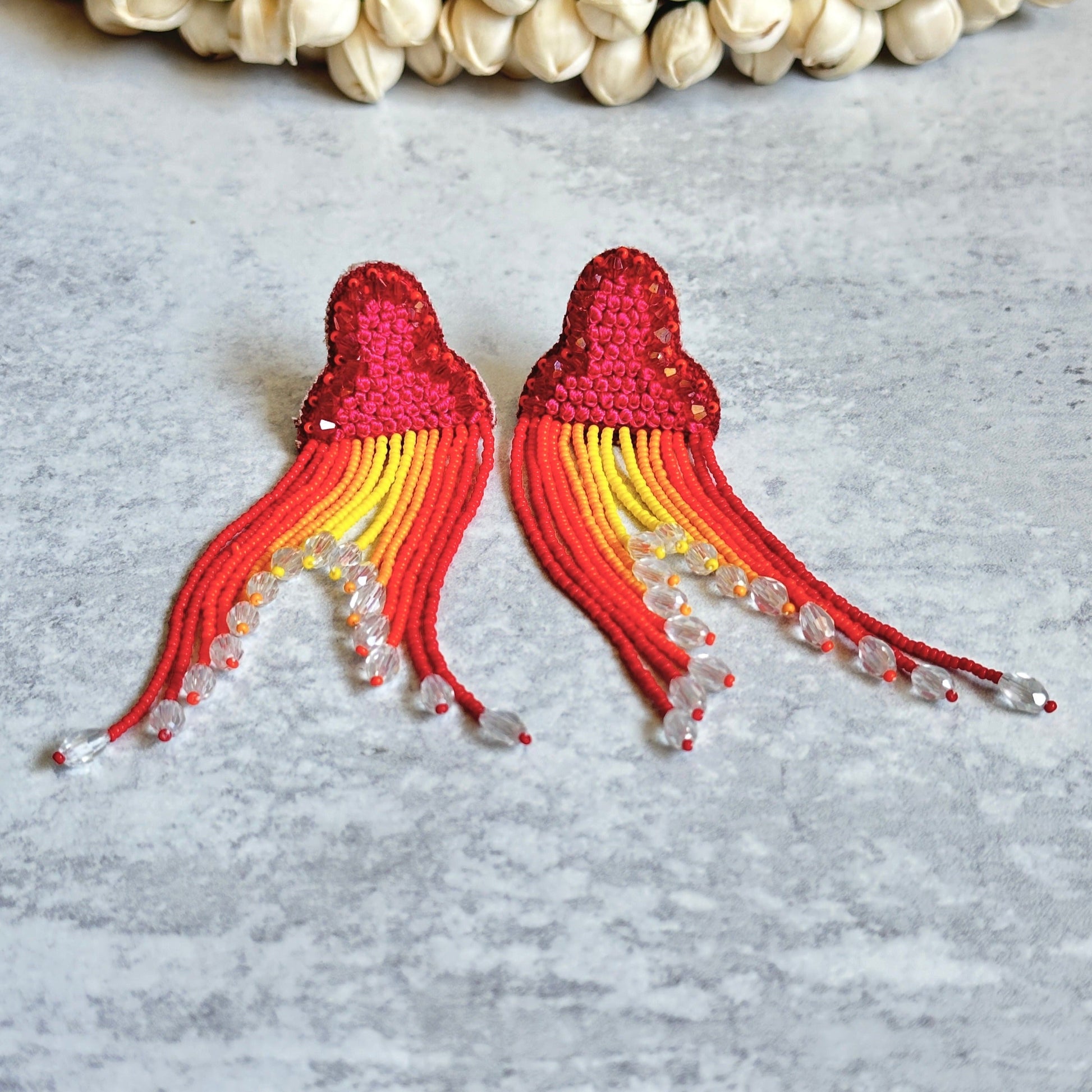 Pair of red, orange, yellow tassel earrings on grey background.