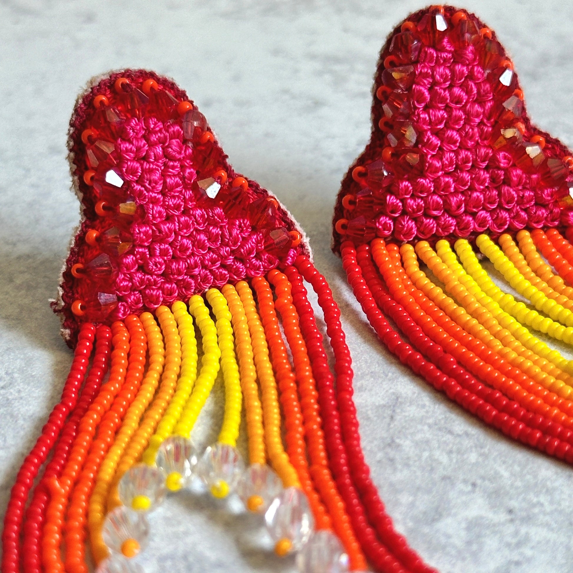 Closeup of Pair of red, orange, yellow tassel earrings on grey background.
