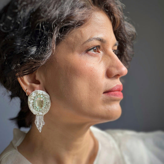 Right front view of woman wearing Pair of iridescent white earrings with pink and blue accents.