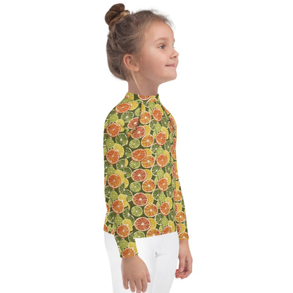 A kids’ citrus rash guard with playful orange and green fruit motifs on a white base, shown from the side.