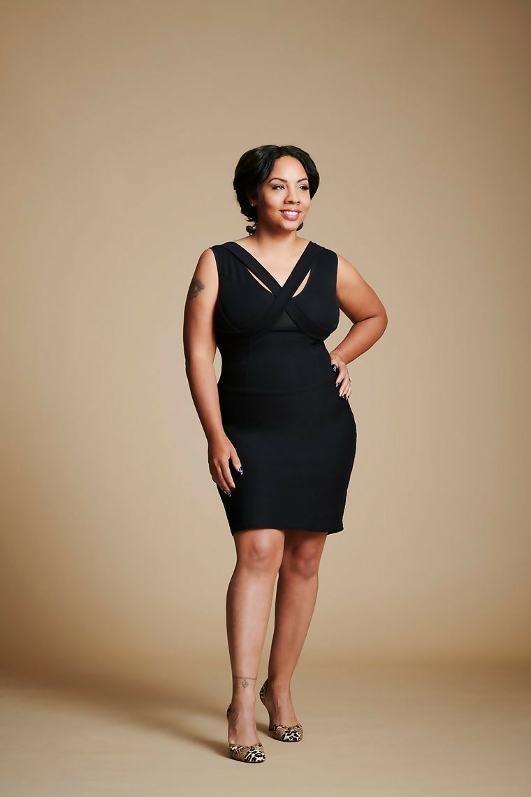 Women posed with left hand at waist, right leg slightly forward, wearing a black dress.