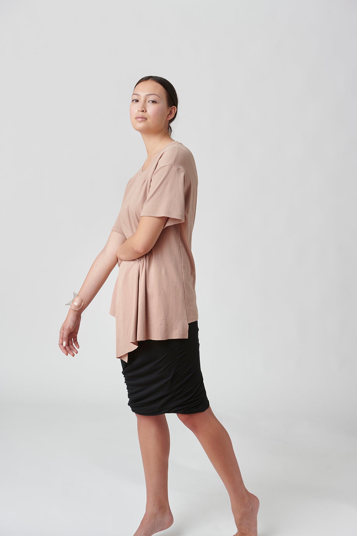 Left front view of woman wearing taupe tee and black skirt.