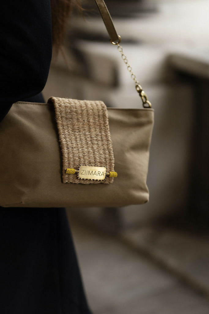 Shadowy view of sandstone green bag with brass details hanging from woman's right shoulder.