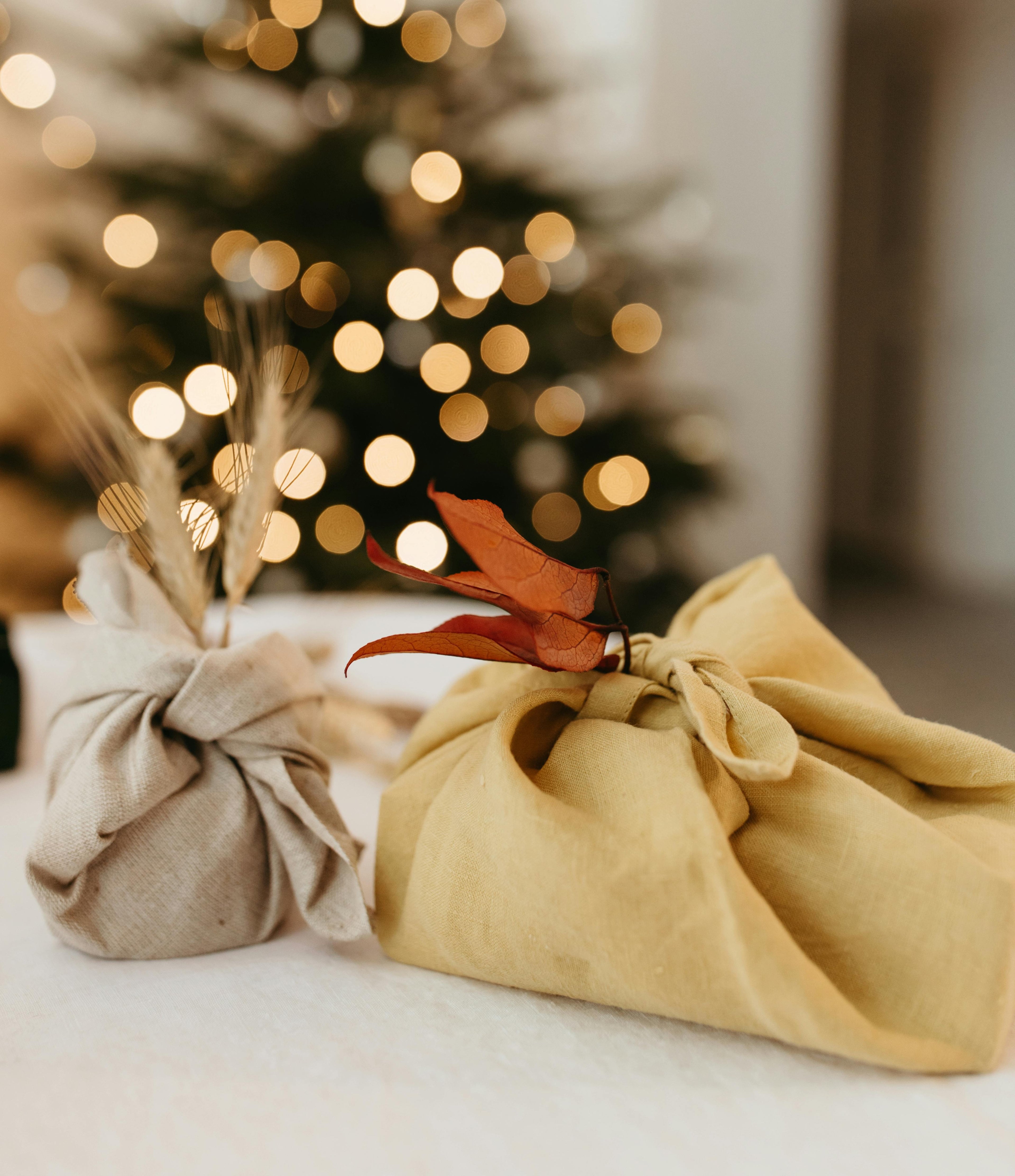 Two wrapped presents with decorative elements in front of a blurred Christmas tree.
