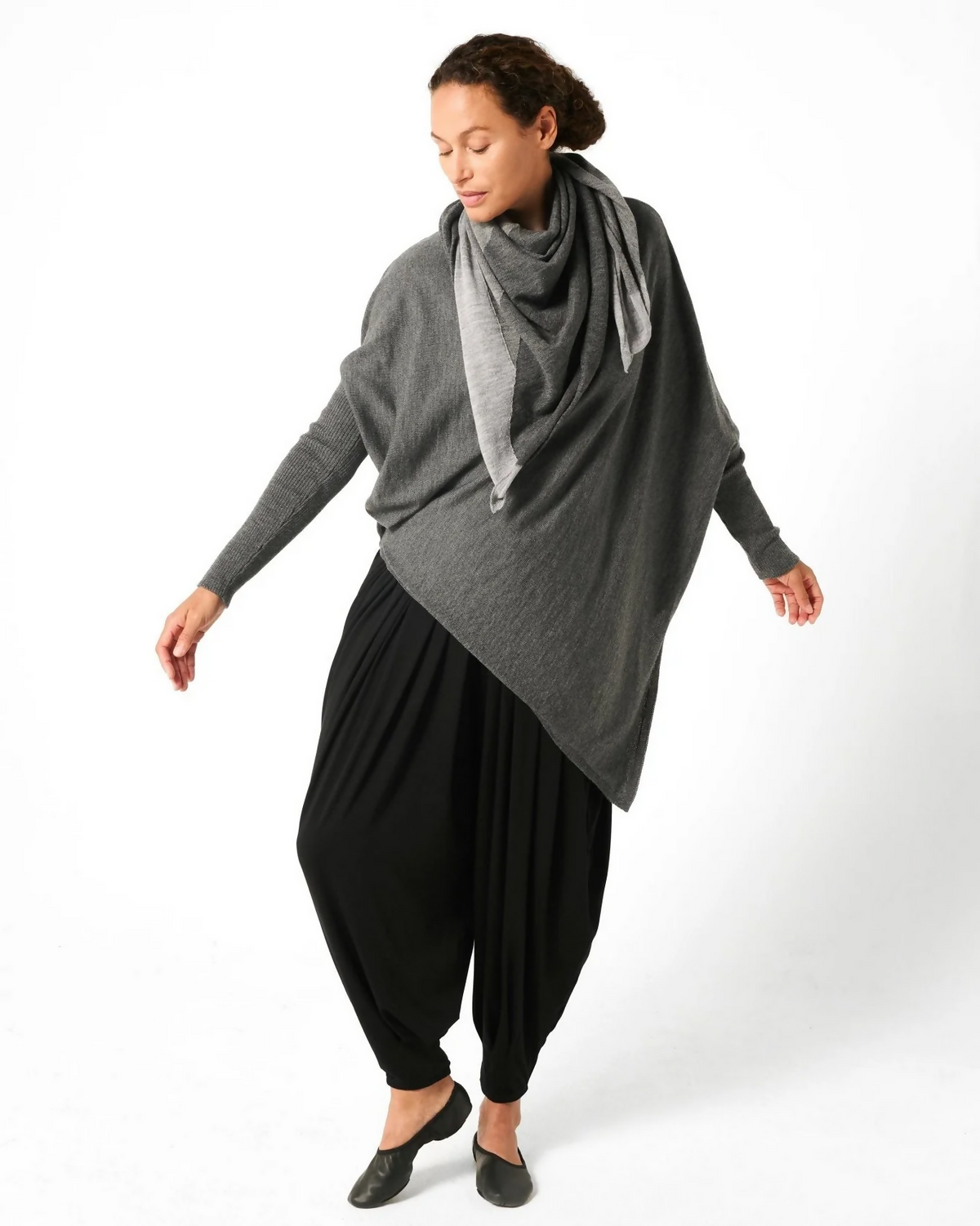 Woman wearing grey drape sweater with black baloon pants and black and grey scarf.