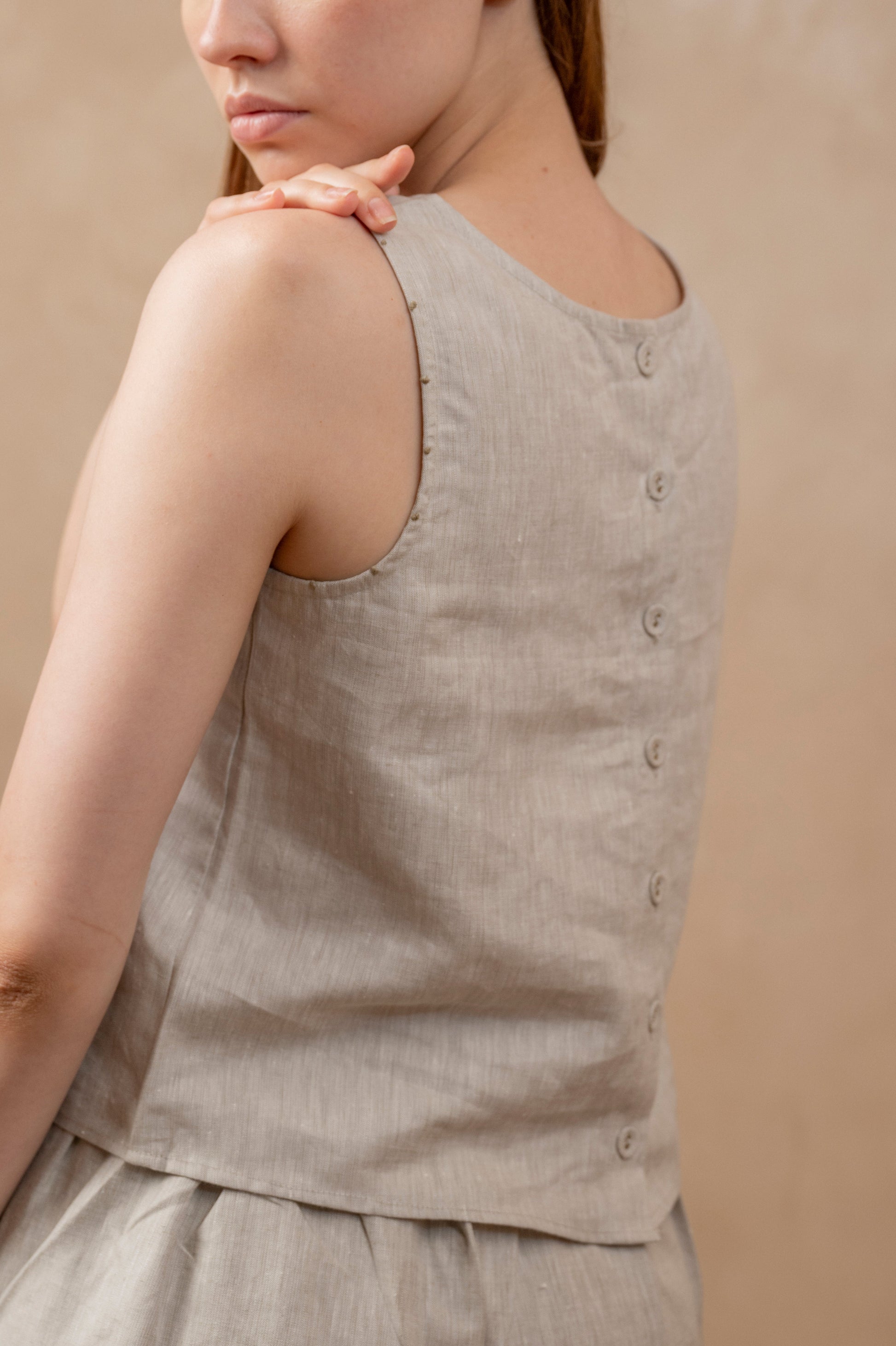 Back view of woman looking over left shoulder, wearing Tulua Women's Sleeveless Top, Natural Hemp Sustainable Fabric,  Back Side, Close up, buttons.