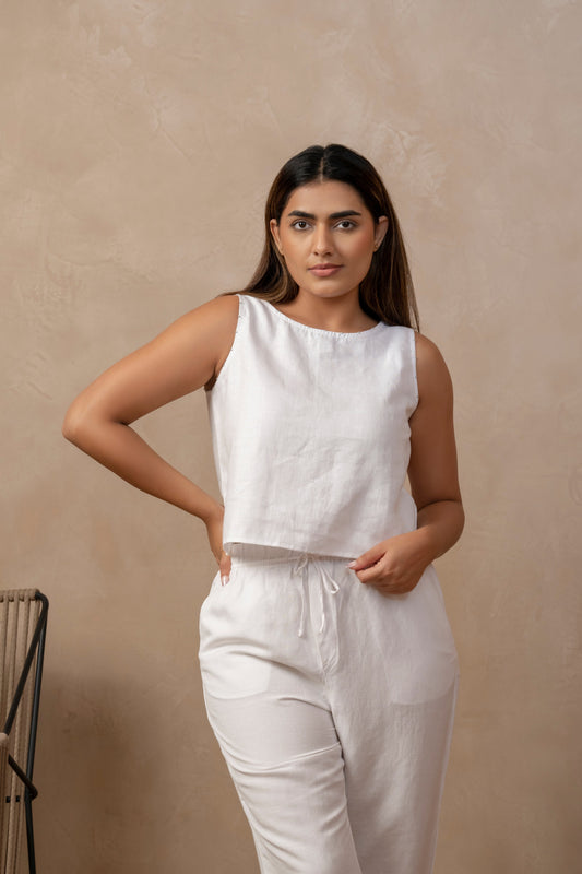 Front view of woman wearing Taru | Sleeveless Top in White and matching white pants, right hand on waist, left hand holding fabric.