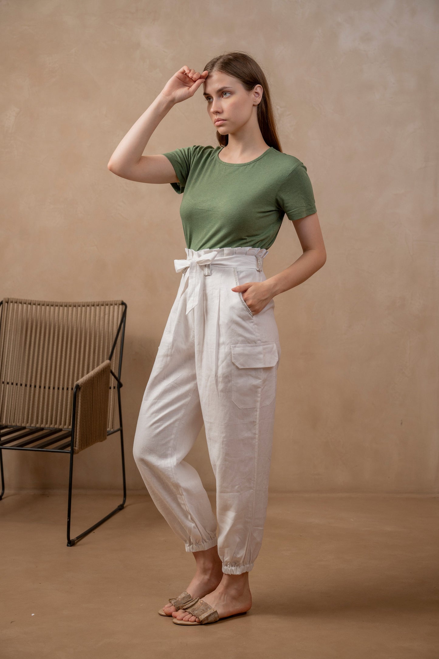 Woman wearing Yama | Cargo Jogger Pants in White, waistband tied in bow and green shirt.  Left hand is in pocket, right hand is at forehead.