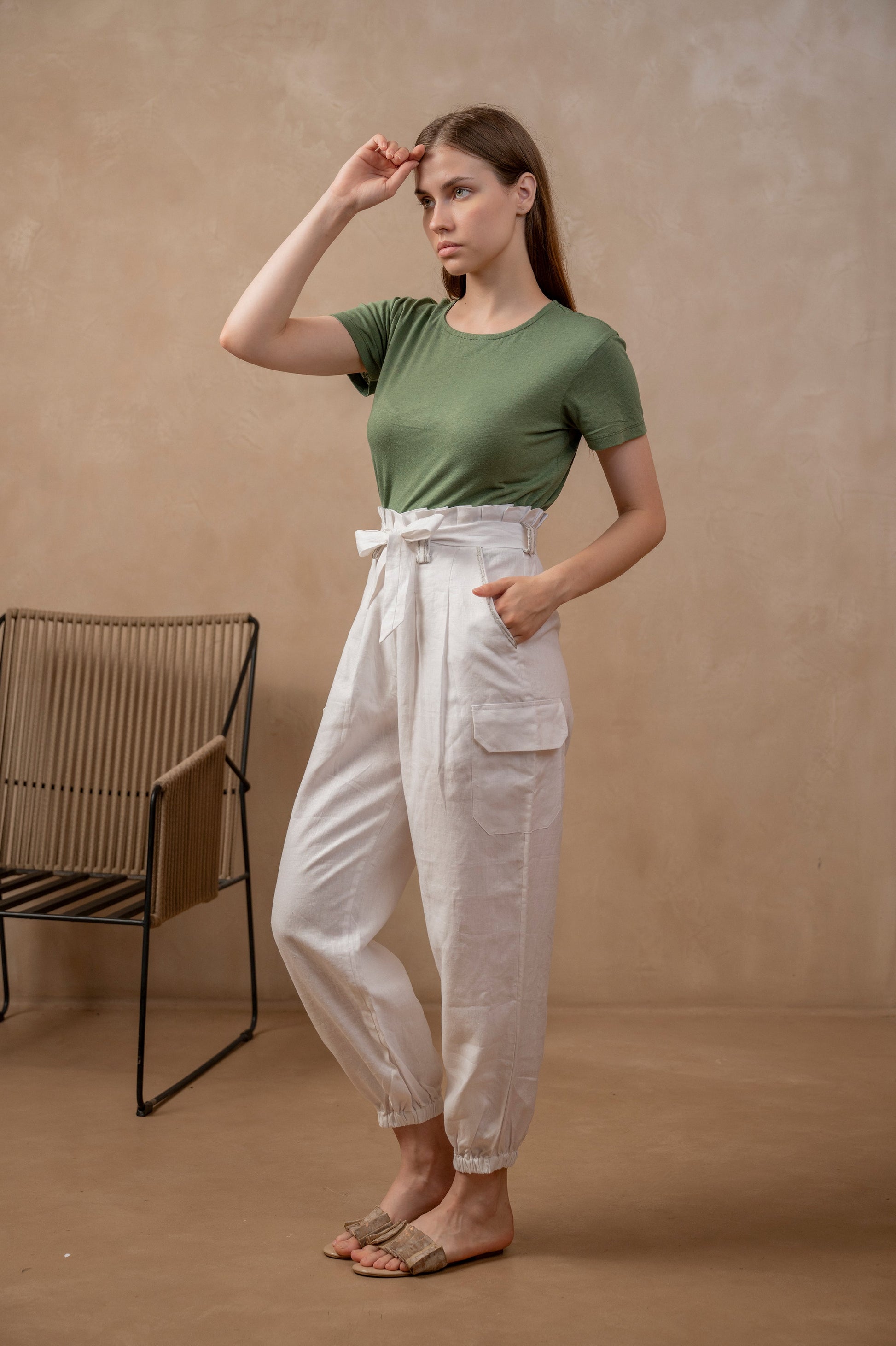 Woman wearing Yama | Cargo Jogger Pants in White, waistband tied in bow and green shirt.  Left hand is in pocket, right hand is at forehead.