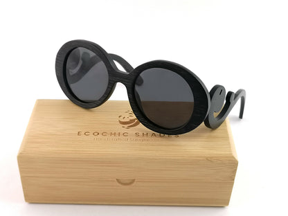 Black bamboo sunglasses with black frames with scroll like design on arms sitting on a rectangular bamboo case.