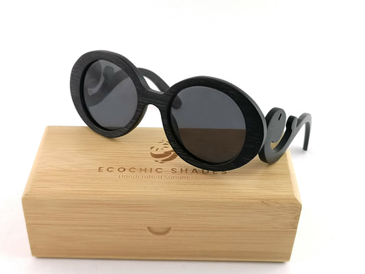 Black bamboo sunglasses with black frames with scroll like design on arms sitting on a rectangular bamboo case.