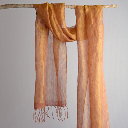 Rust orange handwoven linen scarf with gold zari metallic threads, dyed with natural myrobalan and tea, hanging on a white background.