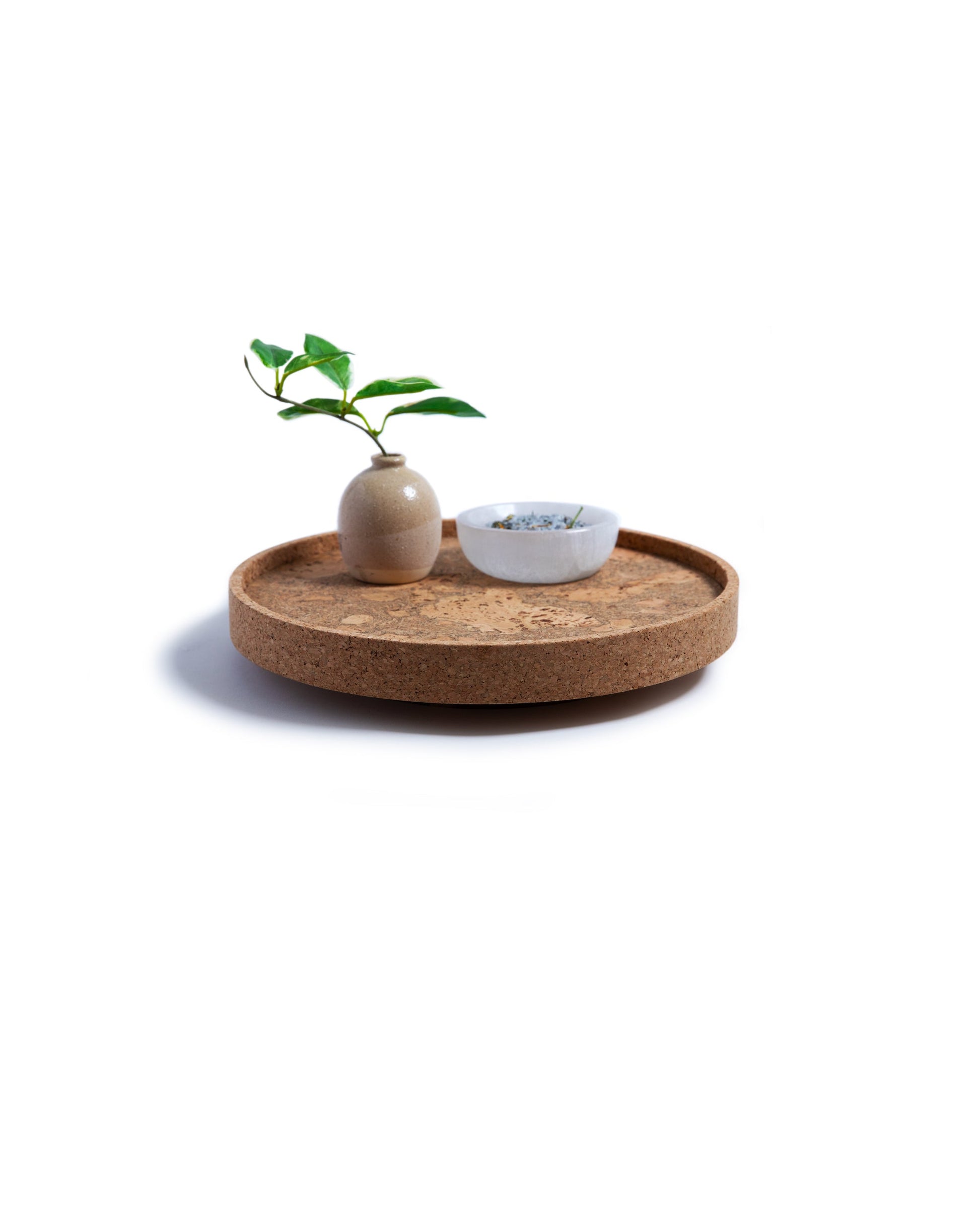 Side view of a circular cork Lazy Susan spinning tray with acacia wood base with a brown vase with leaves in it and a white bowl on top.