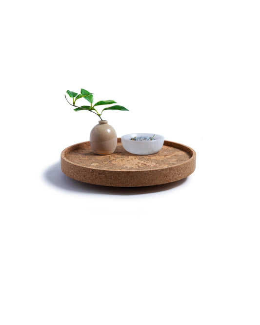 Side view of a circular cork Lazy Susan spinning tray with acacia wood base with a brown vase with leaves in it and a white bowl on top.