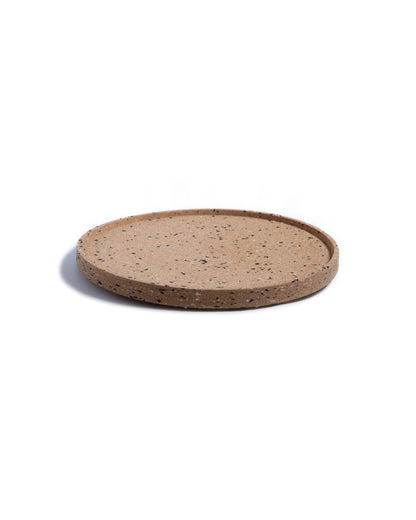 Side view of round cork serving tray with black and grey confetti bits of recycled plastic.