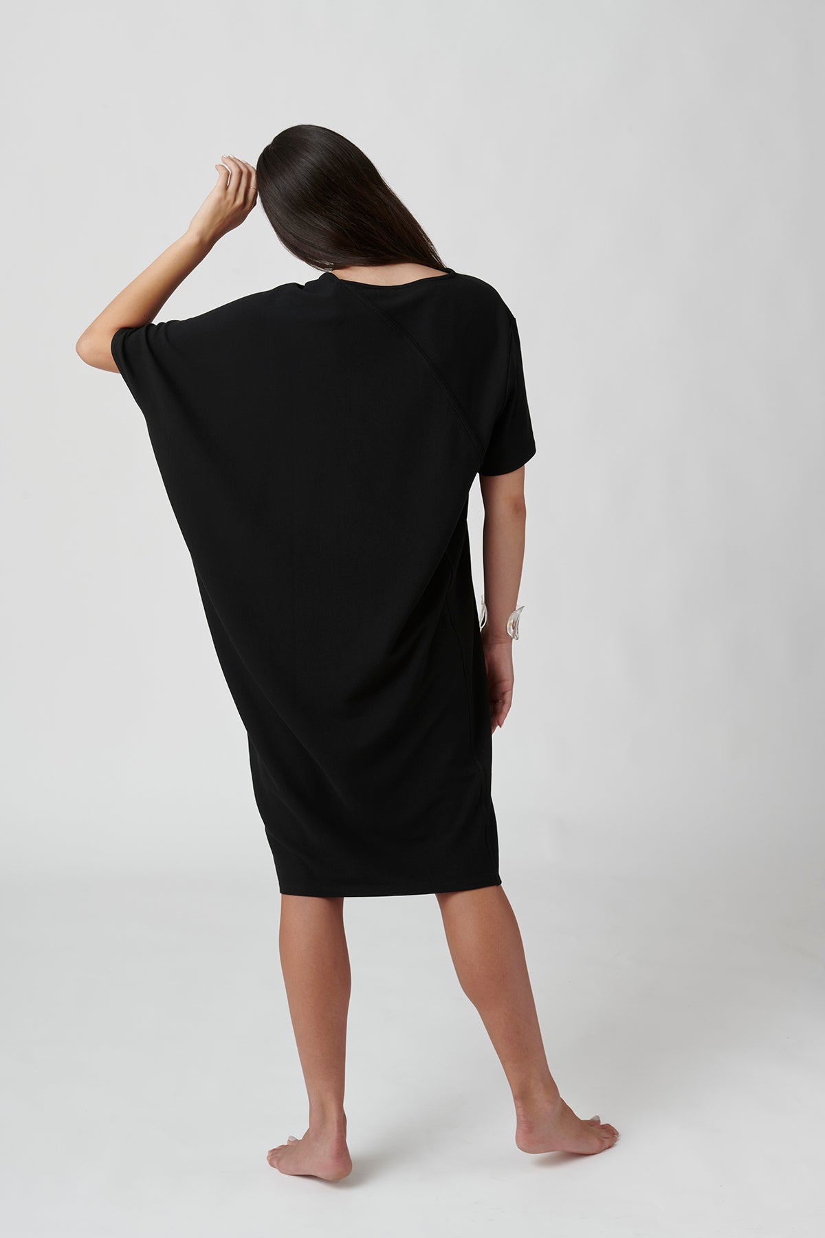 Back view of woman wearing black dress, left hand on head.