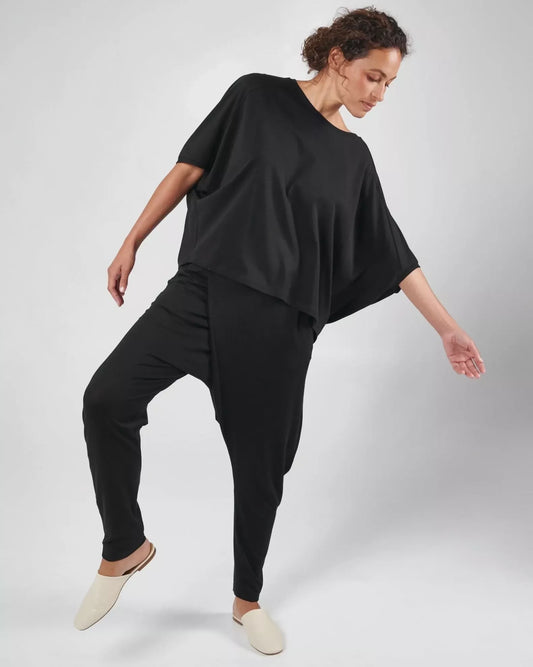 Woman wearing drapey black organic cotton top, bending sideways.