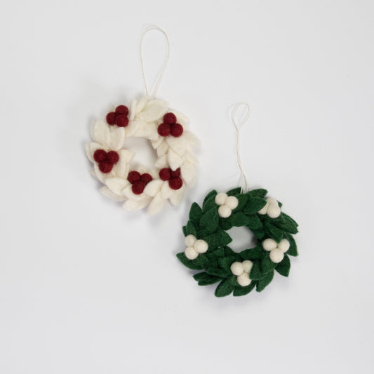 Felt ornaments of mini wreaths, one in white with red berries and the other in green with white berries.
