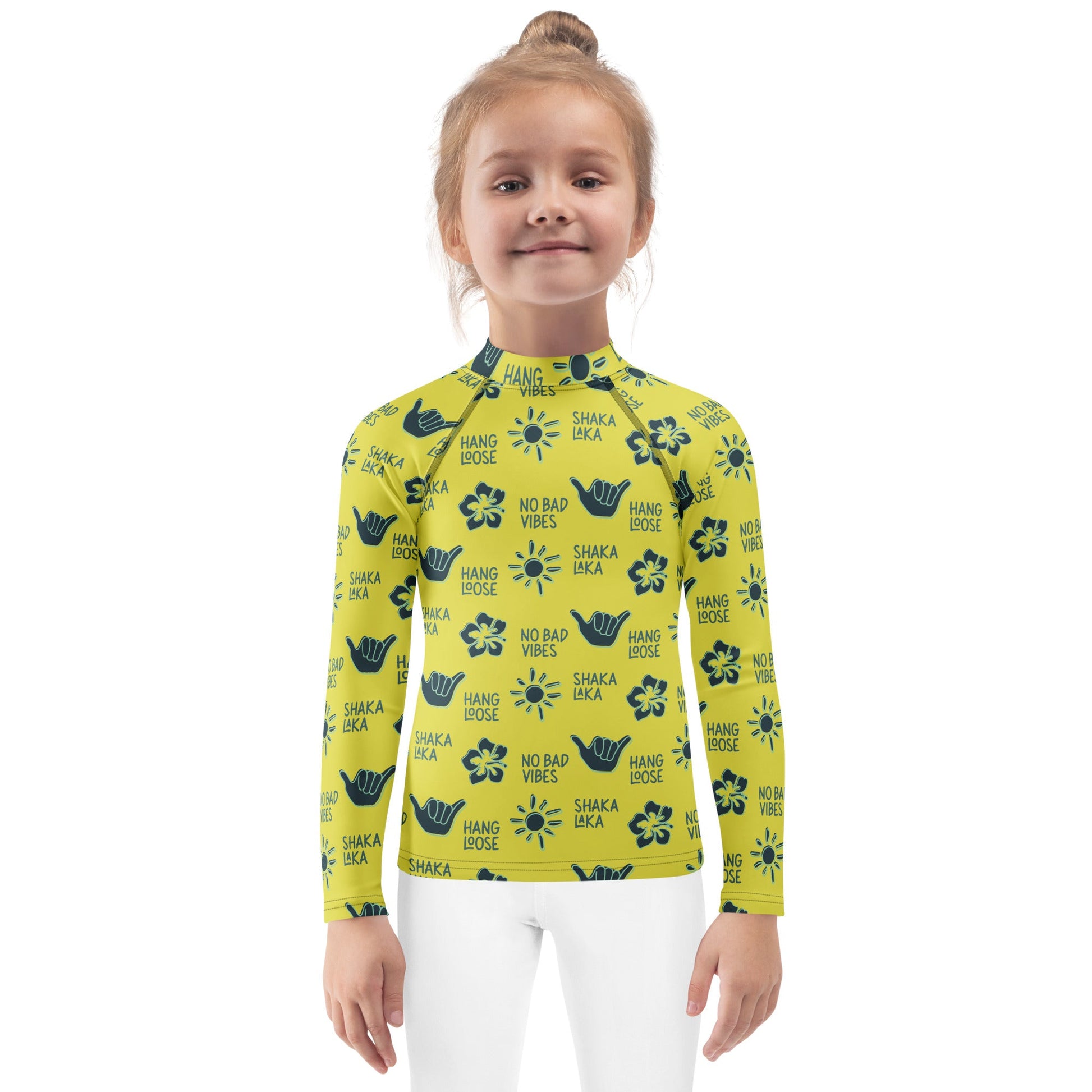 Little girl wearing a yellow rash guard with navy designs of the  sun, hibiscus flowers, hang loose hand sign, and the words hang loose, no bad vibes, and shaka laka.